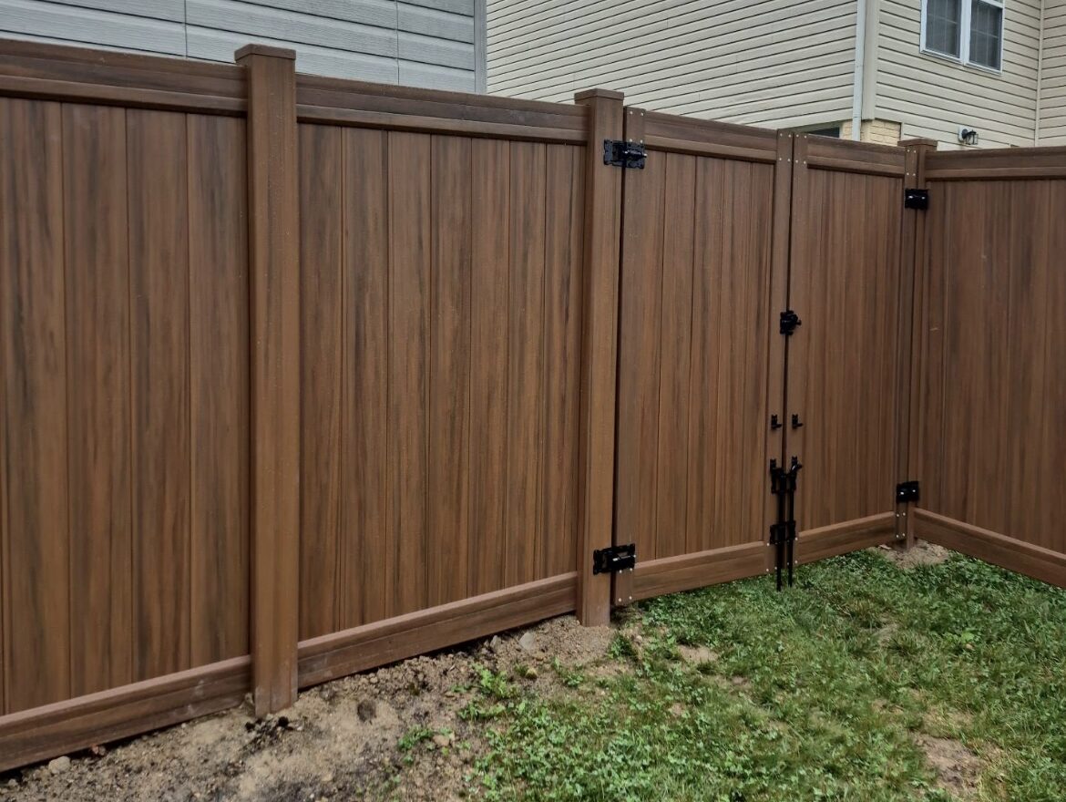Woodgrain vinyl privacy fence with a walk gate beside a house, installed by Future Solutions Fence
