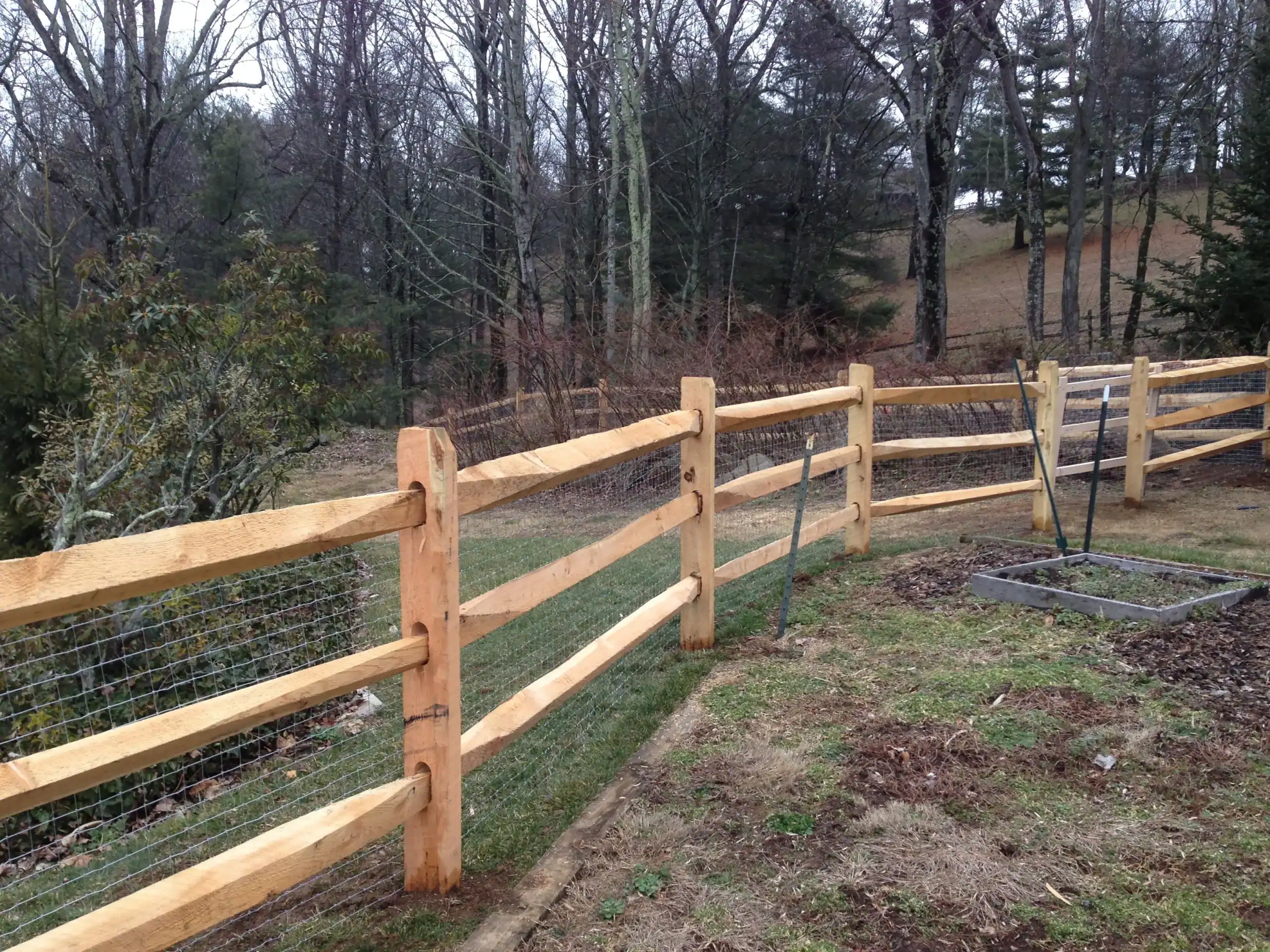 Three-rail split rail fence with wire mesh backing along a wooded property line, installed by Future Solutions Fence