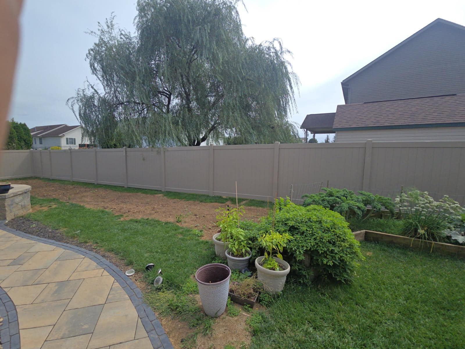 Tan vinyl fence behind a planted garden bed, installed by Future Solutions Fence