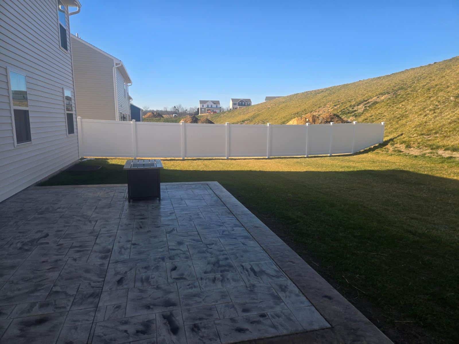 White vinyl fence enclosing a back yard with a paved patio, installed by Future Solutions Fence