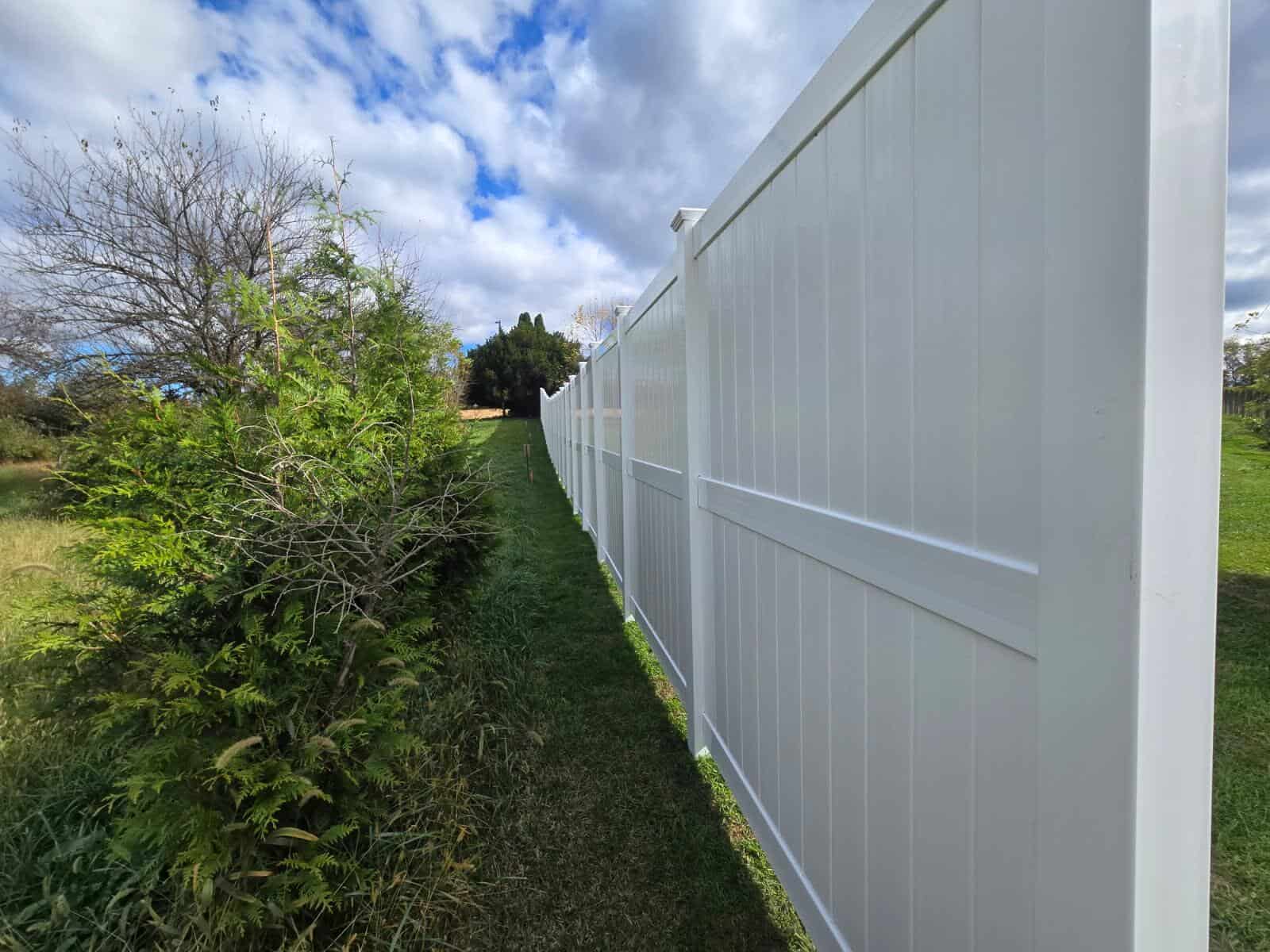 White vinyl fence running along a line of trees, installed by Future Solutions Fence