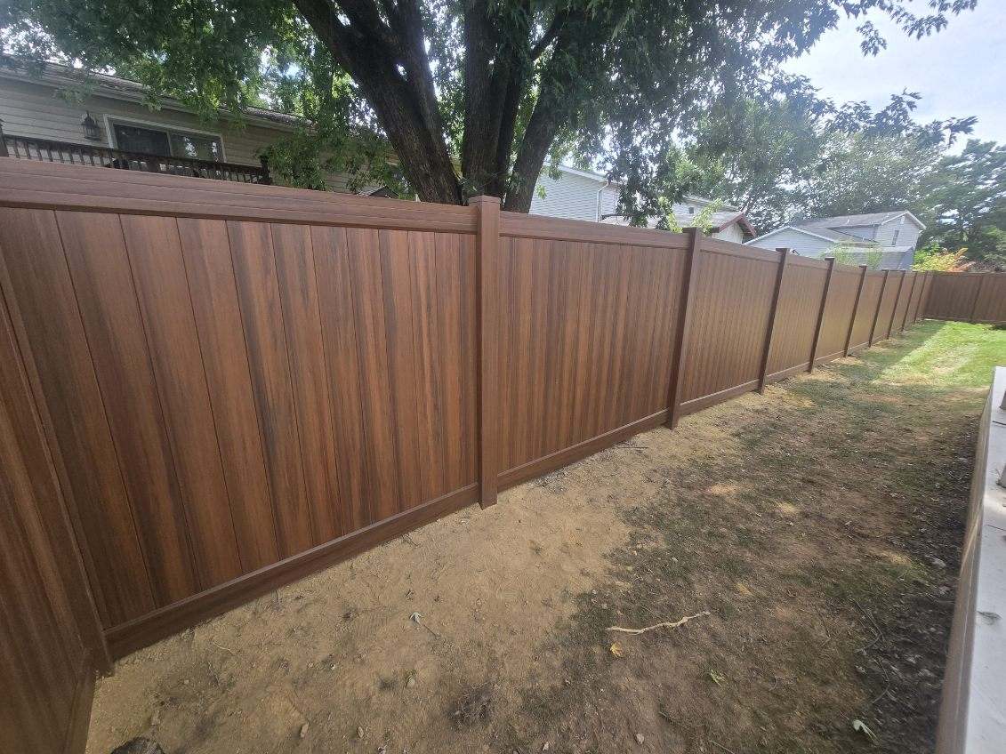 Mocha walnut woodgrain vinyl privacy fence running along a property line, installed by Future Solutions Fence