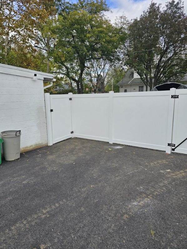 White vinyl privacy fence with a walk gate at the edge of a lawn, installed by Future Solutions Fence